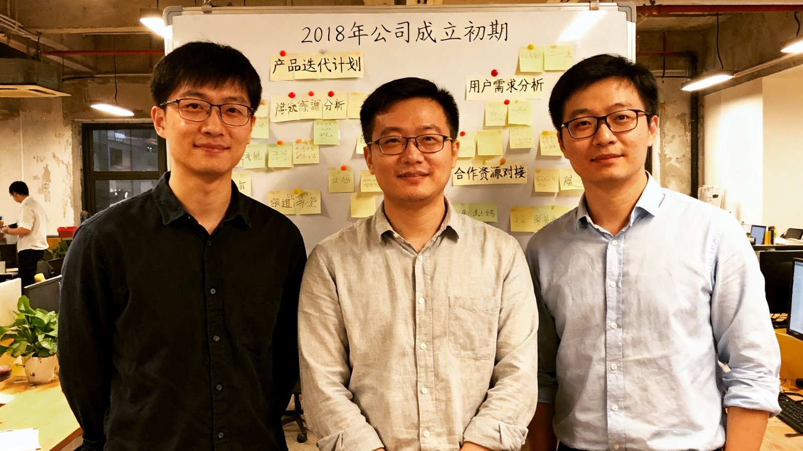 极速直播三位创始人在2018年公司成立初期的合影，背景是简陋的共享办公室和贴满便签的白板